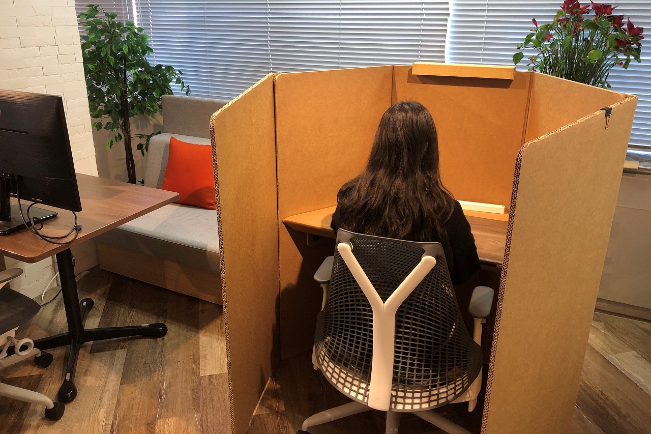 オフィス・ラボが作成したオリジナルダンボールブース「patanto」に向かって座っている女性社員の写真